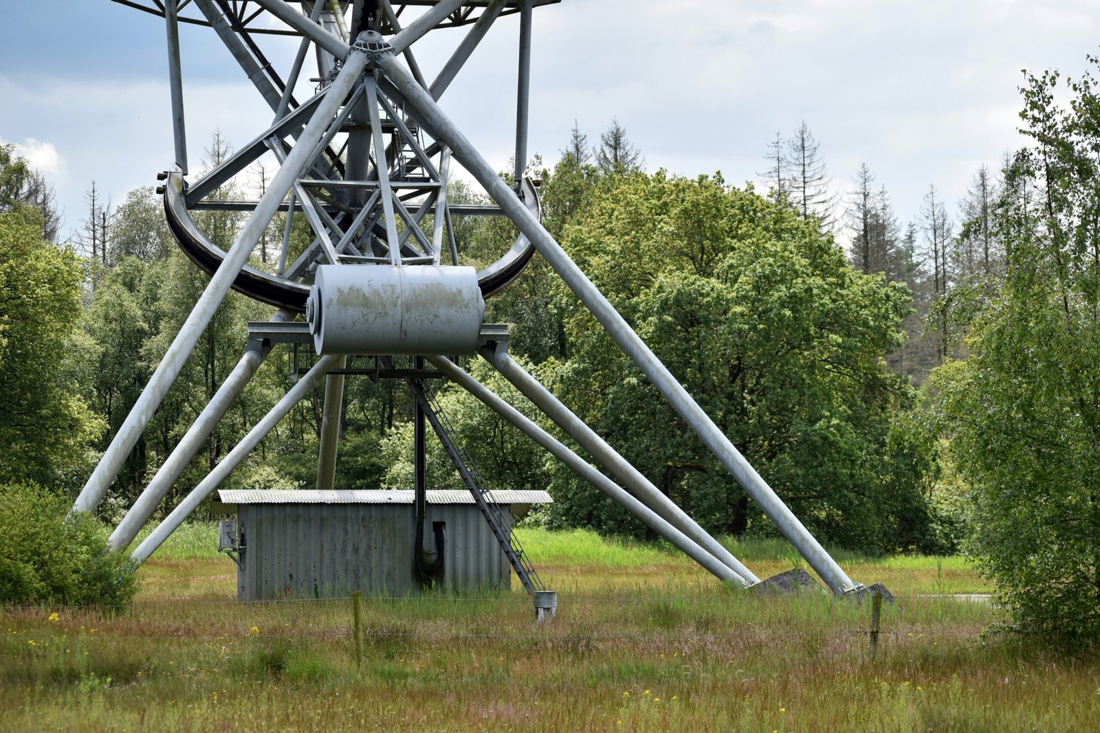 A large metal structure in a field with trees in the background